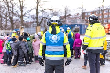 Työvaatteisiin pukeituneita aikuisia ohjeistamassa lapsia