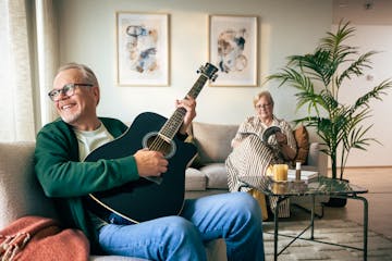 Mies soittaa kitaraa sohvalla